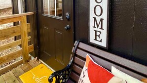 A dark wooden door with a window, a welcome sign, and a bench with cushions.