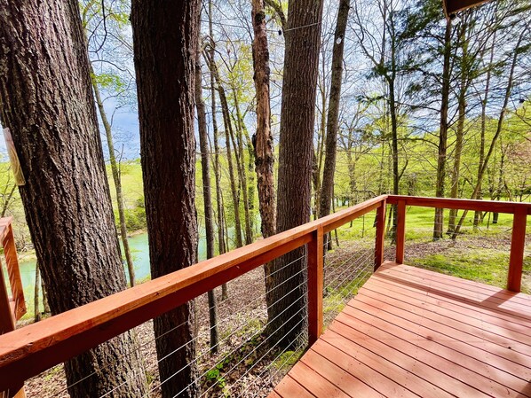 Terraza de madera con barandal de metal que da a un área boscosa con un río.