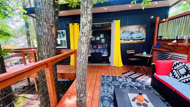 A wooden deck with a sofa and a table, surrounded by trees.
