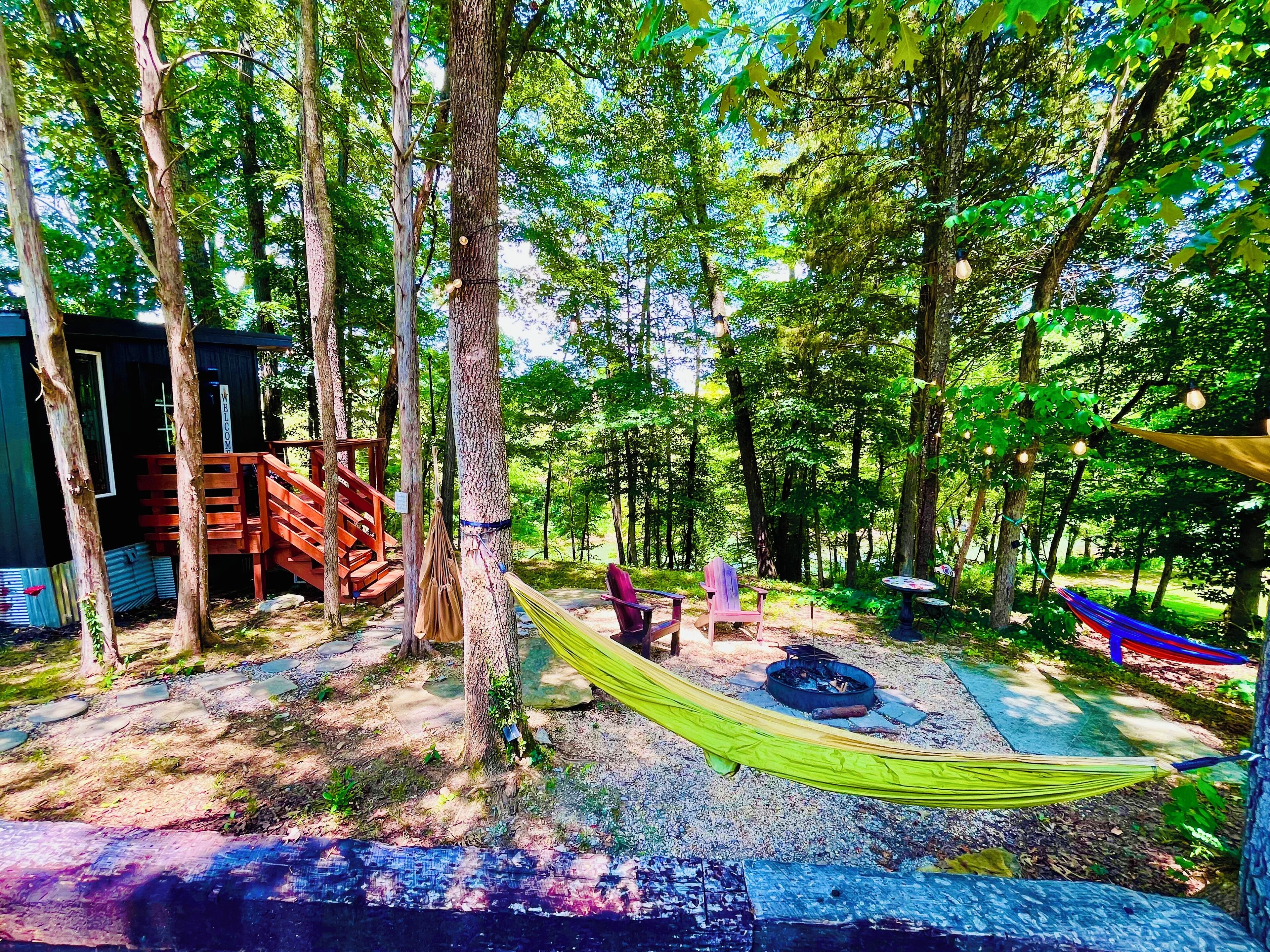 A forested campsite with a wooden cabin, a hammock, and a fire pit.