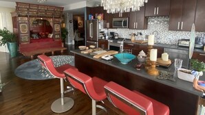 A modern kitchen with dark wood cabinets, a central island with bar stools, a chandelier, and a red sofa in the living area.
