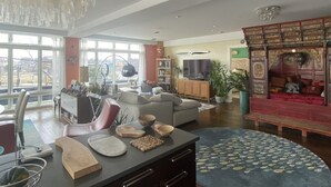 A spacious living room with a large window, a dining area with a kitchen counter, and a traditional red sofa.