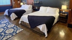 A hotel room with two beds, a wooden floor, a blue wall, and a window with blinds. - The Mineral Schoolhouse (Mineral)