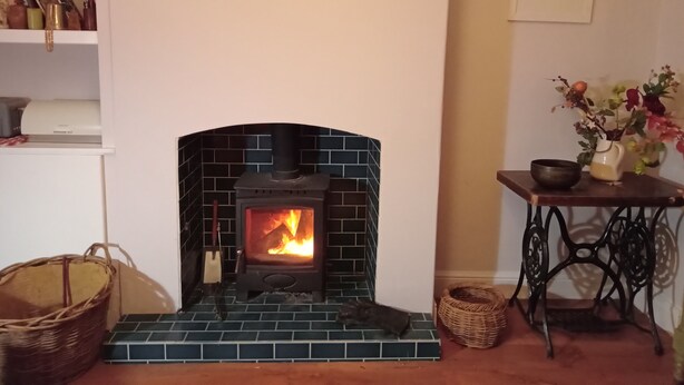 A fireplace with a tiled surround, a shelf with books and decorative items, and a table with a vase and a bowl.