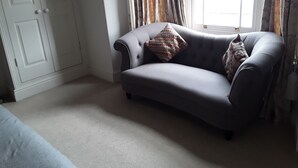 A room with a grey sofa, a white door, and a window with curtains.