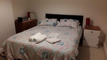 A neatly made bed with floral bedding, a bedside table with a lamp, and a nightstand with a lamp.