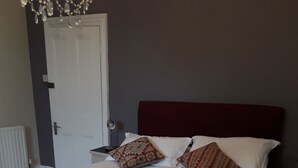 A neatly made bed with white linens and two decorative pillows, a bedside table with a lamp, and a door in the background.