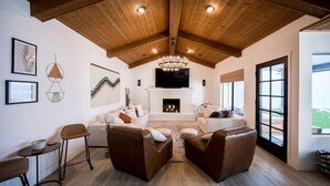 Amplia sala de estar con techo de madera alto, chimenea y televisor grande. Hay dos sofás y una mesa de centro.