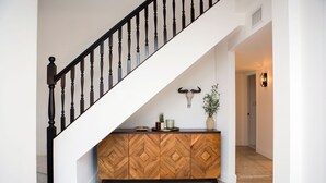Una escalera con detalles de madera y barandales negros, que conduce a una plataforma con un mueble de madera con estampado de espiga y una decoración de cráneo de toro colgada en la pared.
