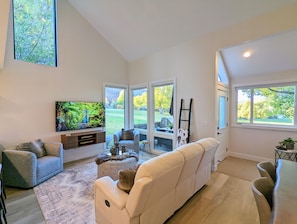 A spacious living room with a large TV, comfortable seating, and large windows offering views of a yard. - Mountain Modern Retreat - Walk to Park City Mtn - 2 King Suites - Pool & Hot Tub (Park City)