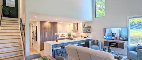 Una cocina moderna con una isla central, un comedor con mesa de madera y una sala de estar con sofá y televisor.