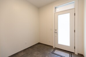 Un couloir avec une porte blanche, un interrupteur et une prise de courant sur le mur.