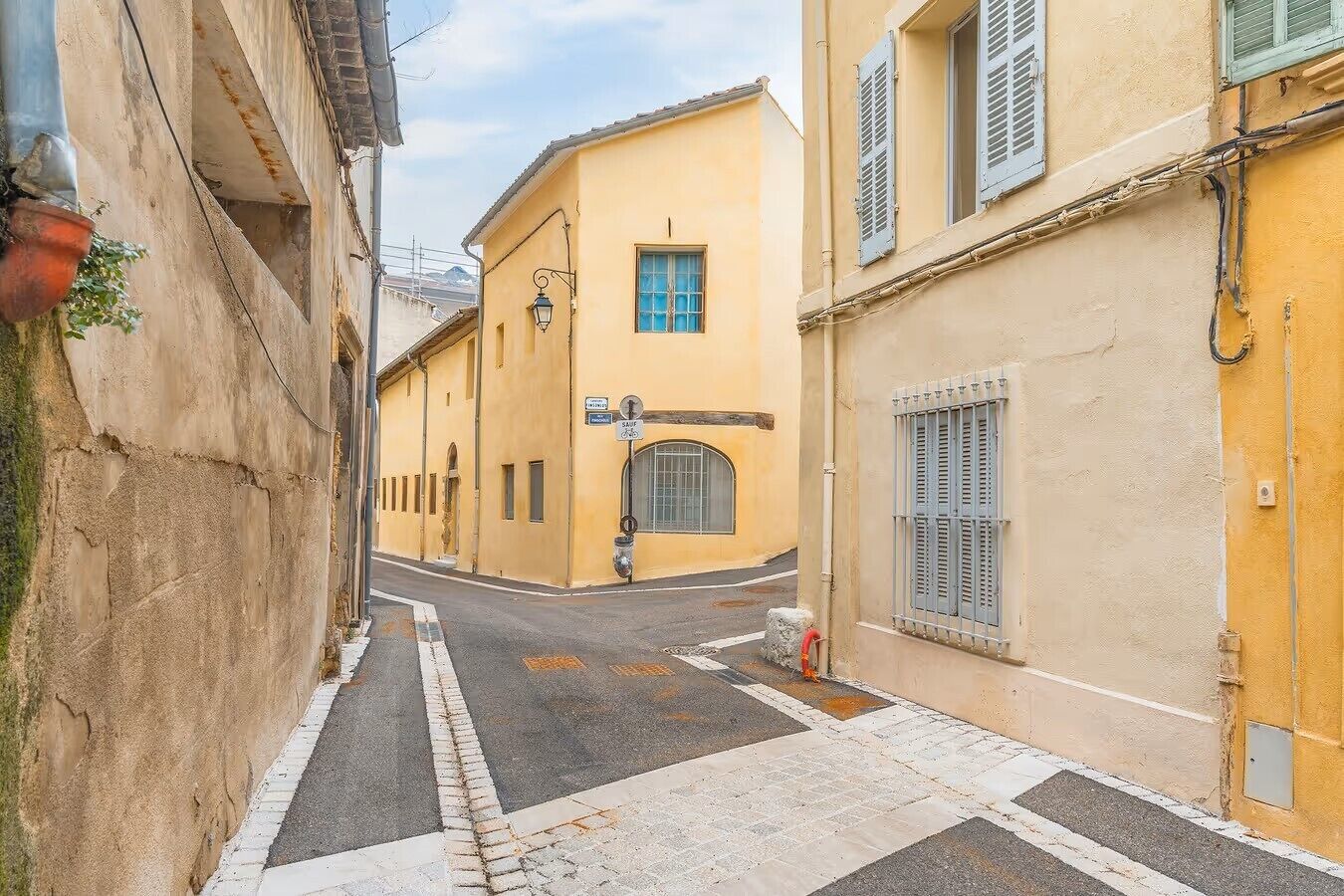 A narrow street with yellow buildings, a visible entrance, and a street lamp.