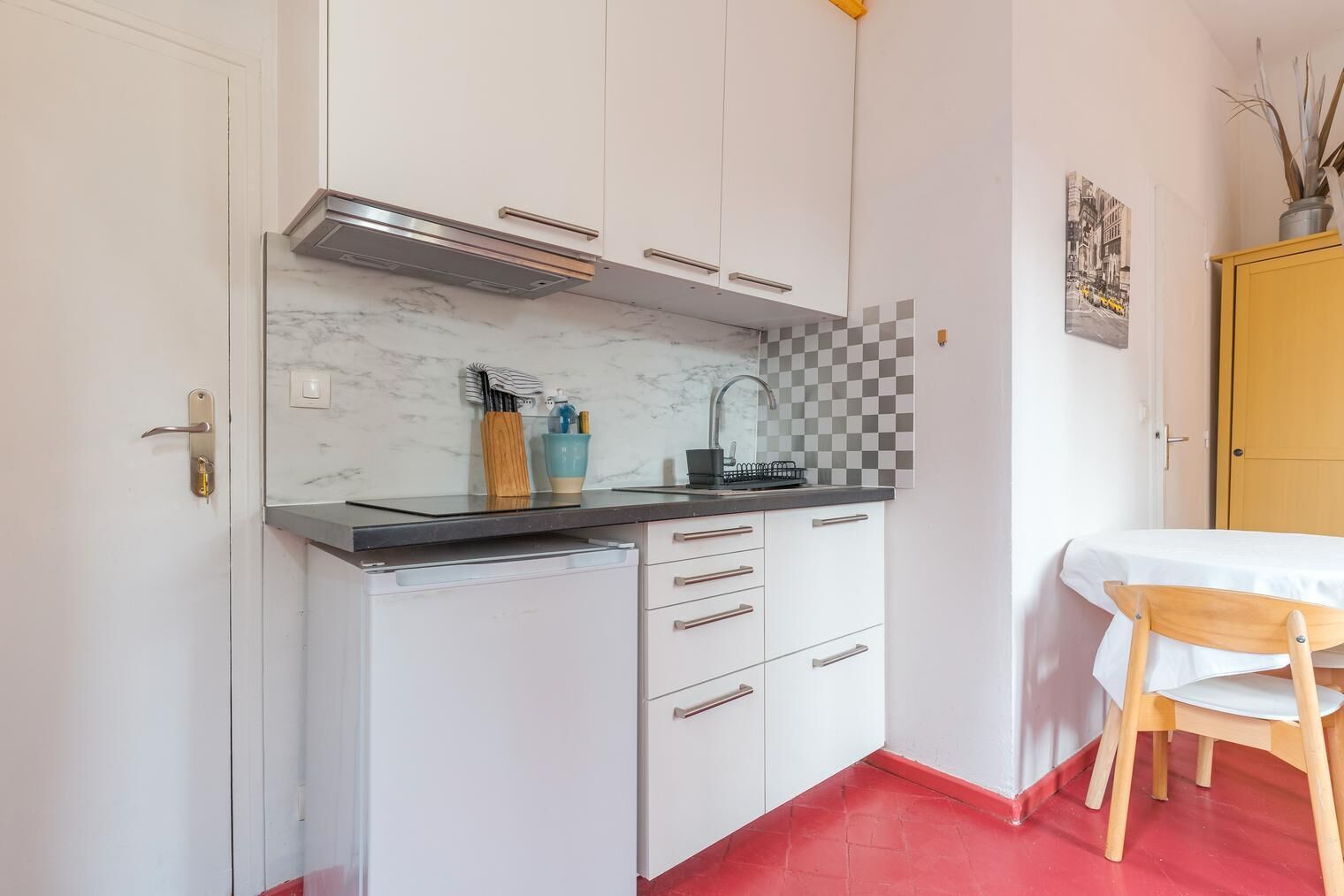 Una cocina pequeña con armarios blancos, encimera negra y suelo rojo.