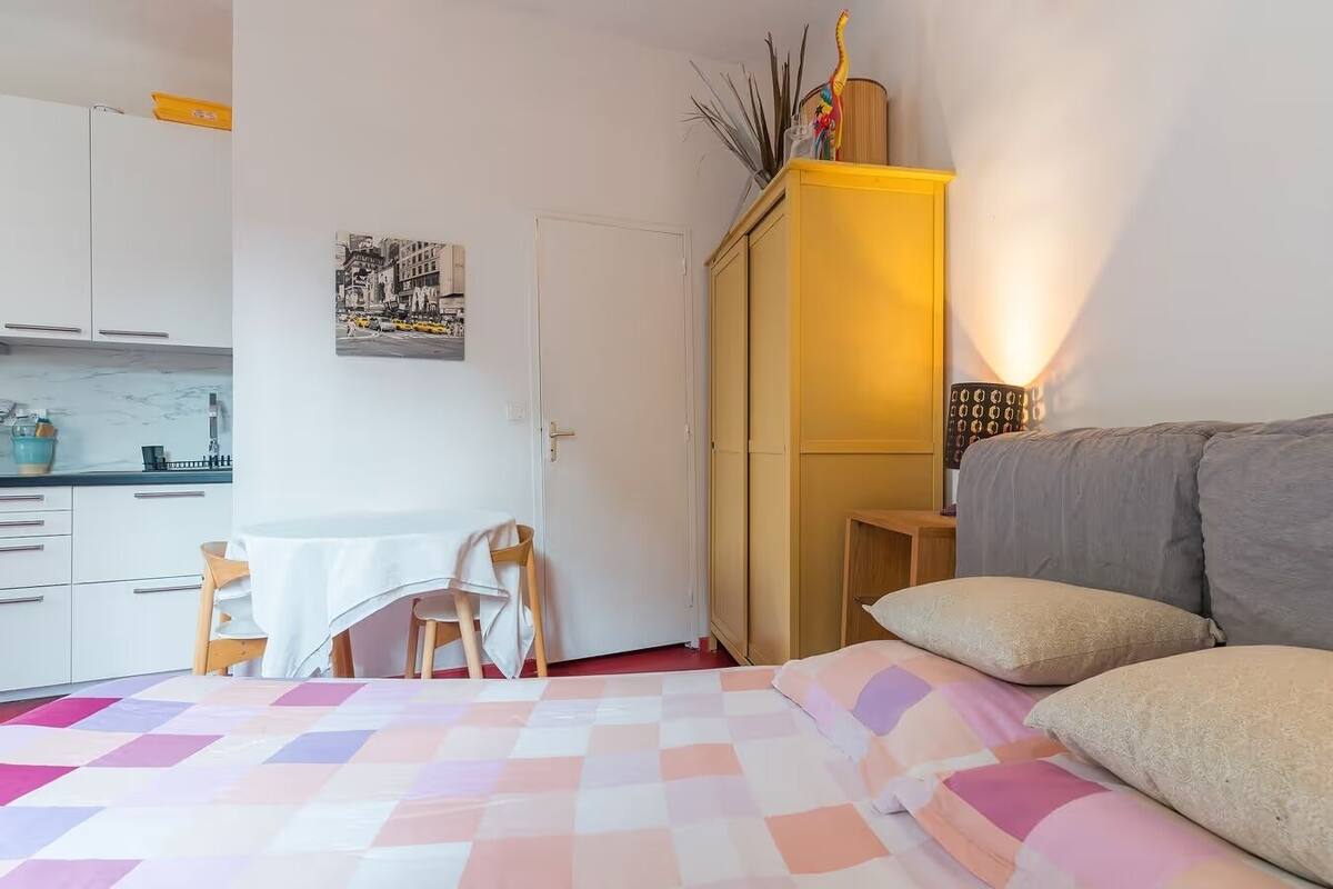 A bedroom with a bed, a desk, and a kitchenette.
