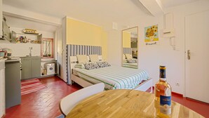 Una habitación de hotel compacta con cama, kitchenette, mesa de comedor y una botella de alcohol.