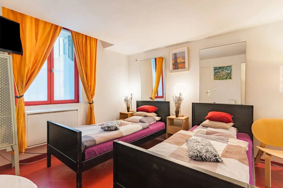 A hotel room with two beds, a TV, a window with curtains, and artwork on the walls.