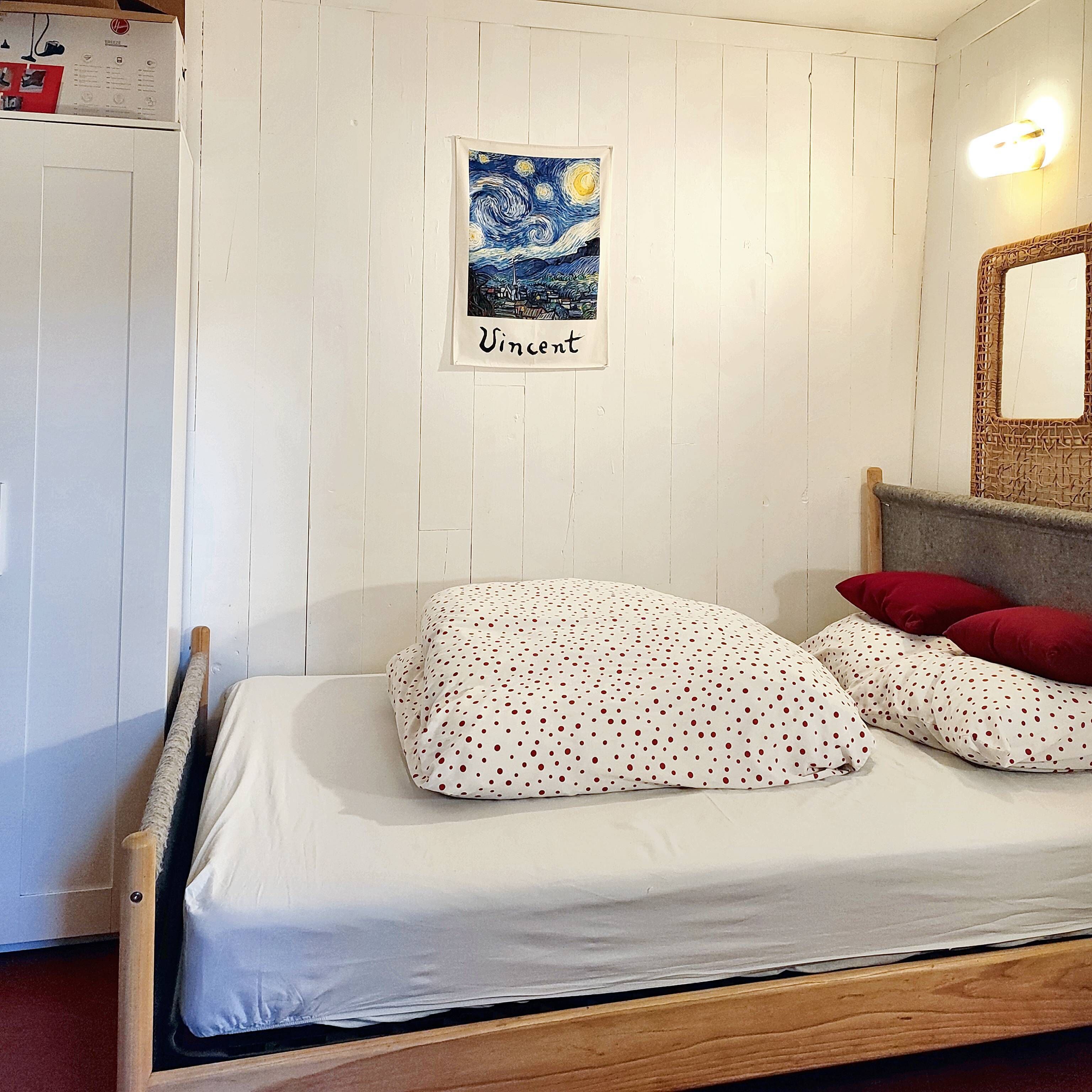 A bedroom with a bed, white polka dot bedding, a framed Vincent painting, and a wooden headboard.