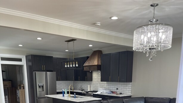 A modern kitchen with dark cabinets, a central island, and a black leather sectional sofa.
