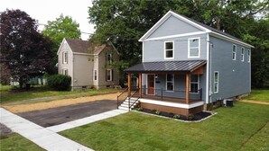 A two-story house with a porch and a small deck, surrounded by a well-maintained lawn and trees.