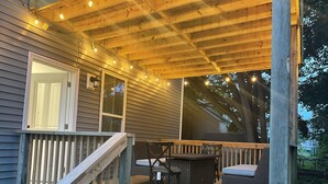 A wooden deck with a covered seating area, a wooden staircase, and string lights.