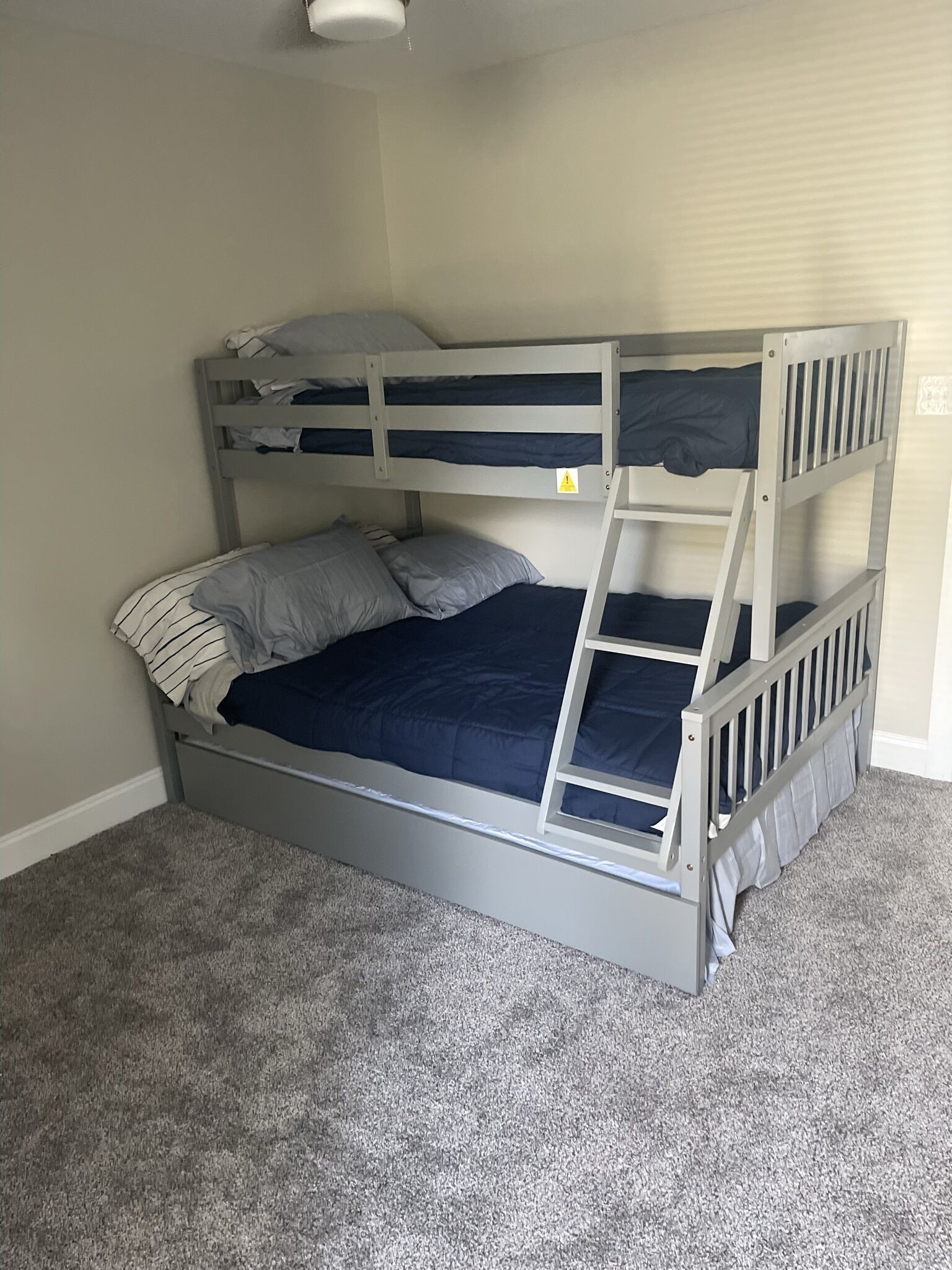 Una cama litera con dos niveles, ropa de cama gris y suelo cubierto de moqueta gris.