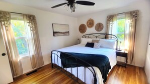 A bedroom with a bed, a ceiling fan, a bedside table with a lamp, and a window with curtains. - Beautiful, Cozy, and Spacious home- 3 mins from downtown (Oberlin)
