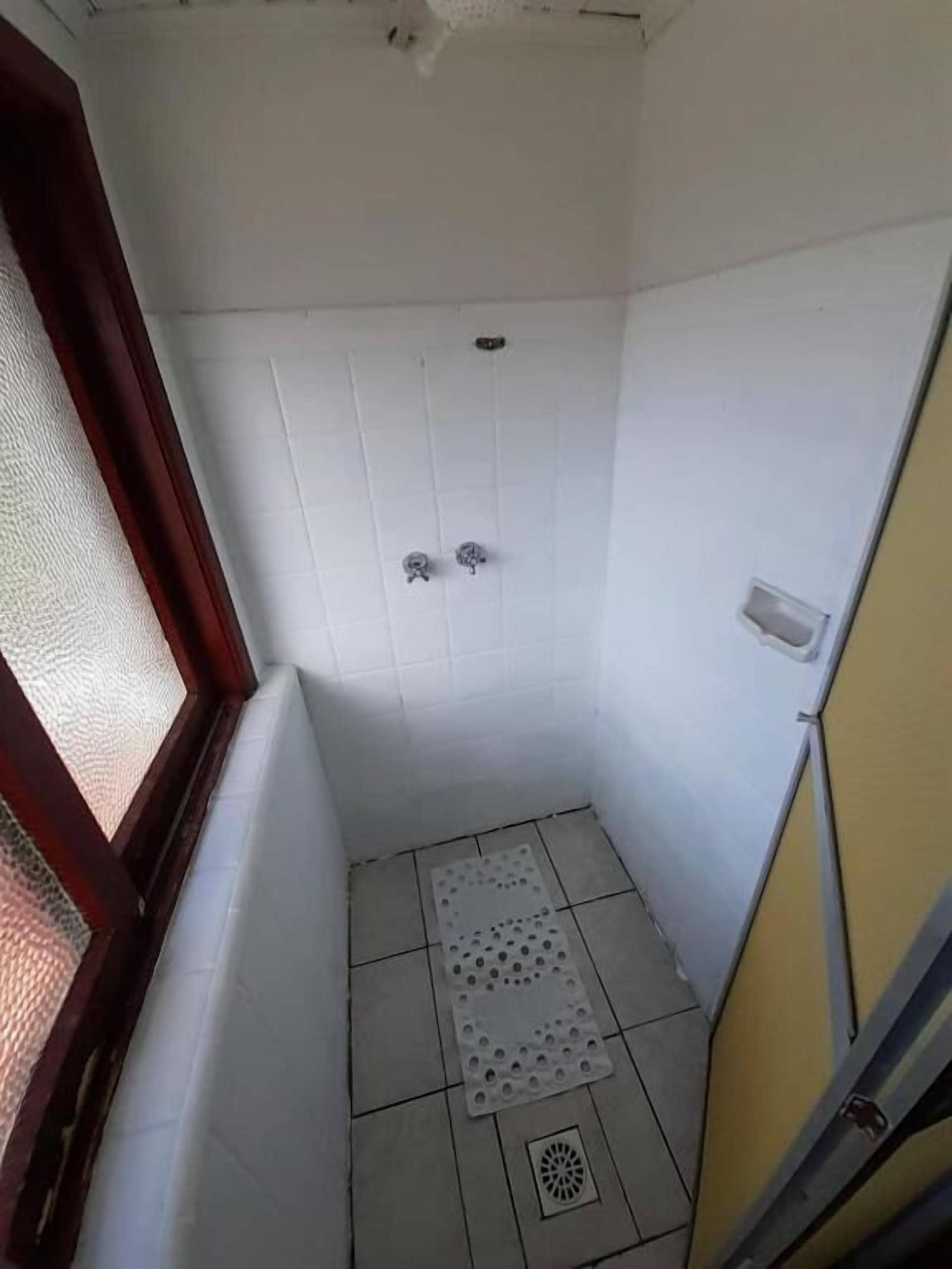 Un baño pequeño y estrecho con paredes de azulejos blancos, una ducha y un inodoro.