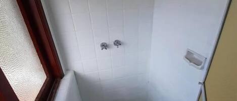 Un baño pequeño y estrecho con paredes de azulejos blancos, una ducha y un inodoro.
