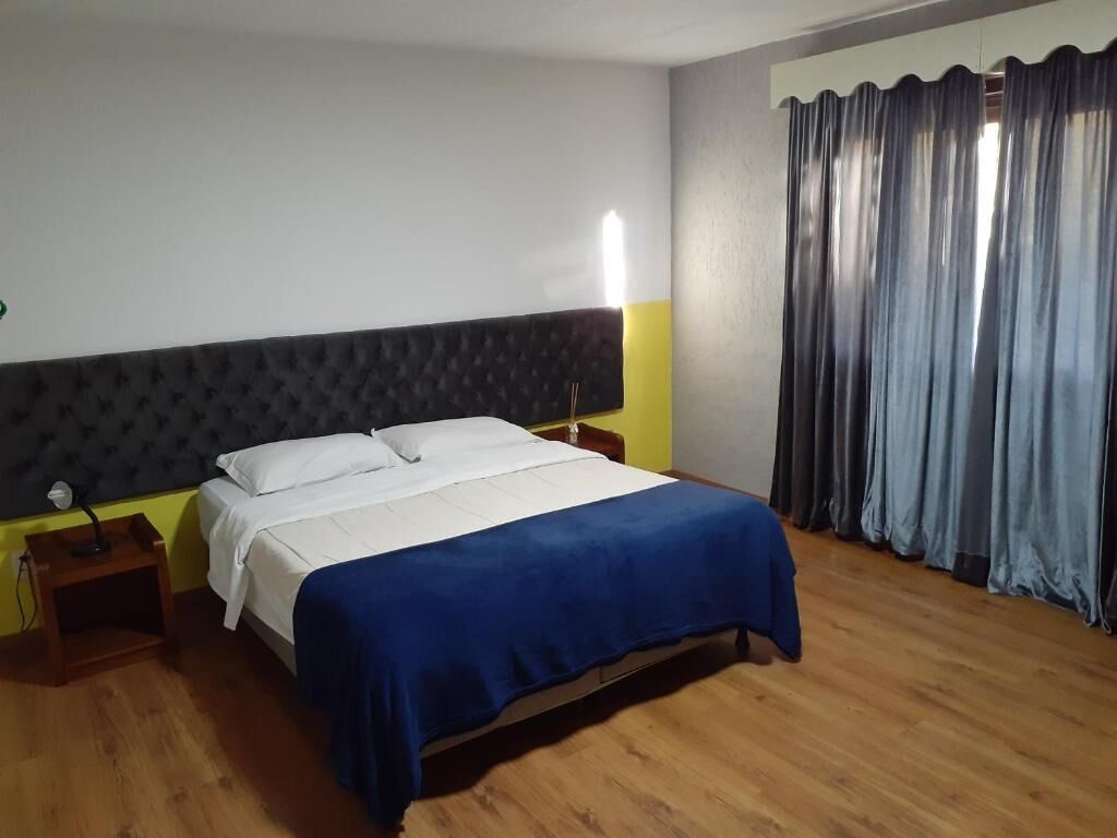 A hotel room with a bed, bedside tables, a nightstand, and a window with curtains.