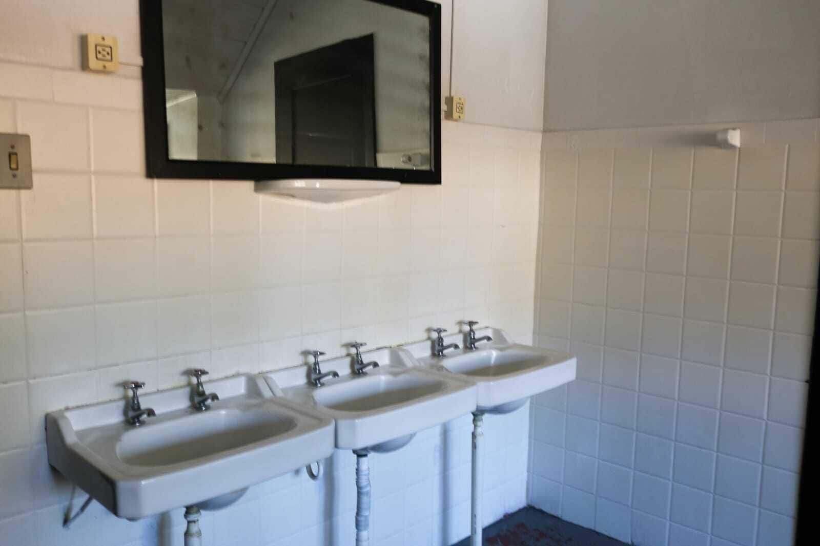 A bathroom with three sinks, a mirror, and white tiled walls.