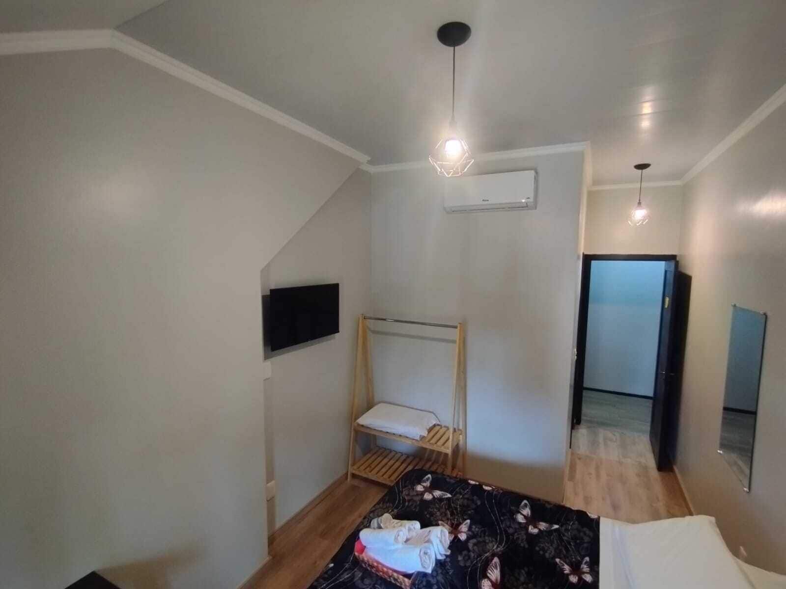 A bedroom with a bed, a TV mounted on the wall, a wooden bed frame, a ceiling light, and a door leading to another room.