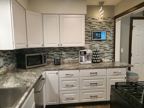 Una cocina con armarios blancos, microondas, tostadora, cafetera y cocina a gas.