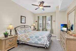 A bedroom with a bed, nightstands, a dresser, a ceiling fan, a TV, and a window with curtains.