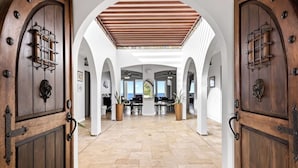 A spacious interior with high ceilings, arched doorways, and a central open area with a piano and dining table.