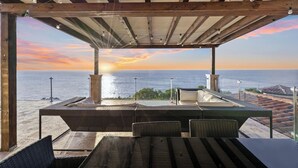 A covered outdoor seating area with a view of the sea at sunset.