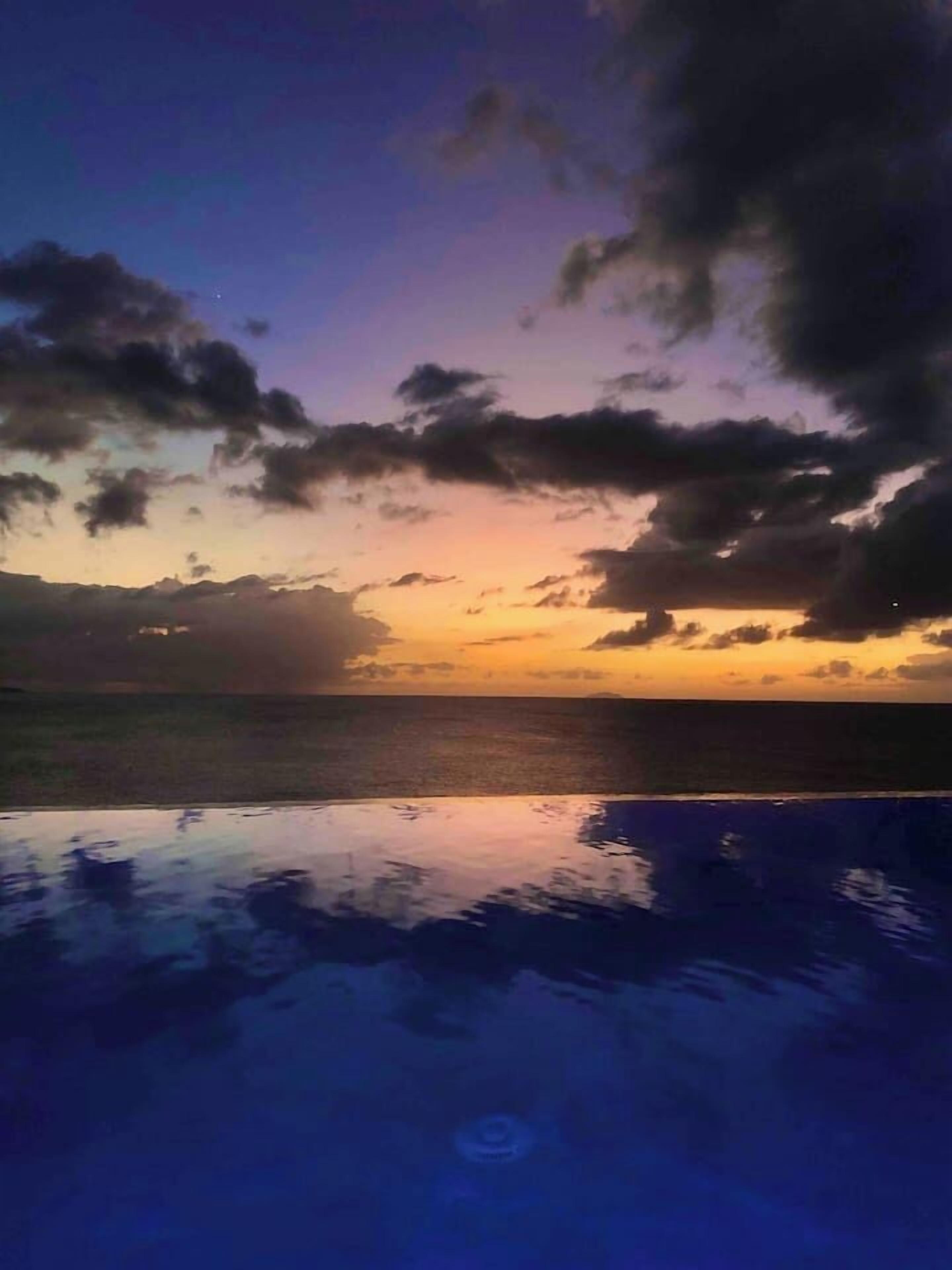 Um pôr do sol sobre a água, com uma piscina ao primeiro plano.