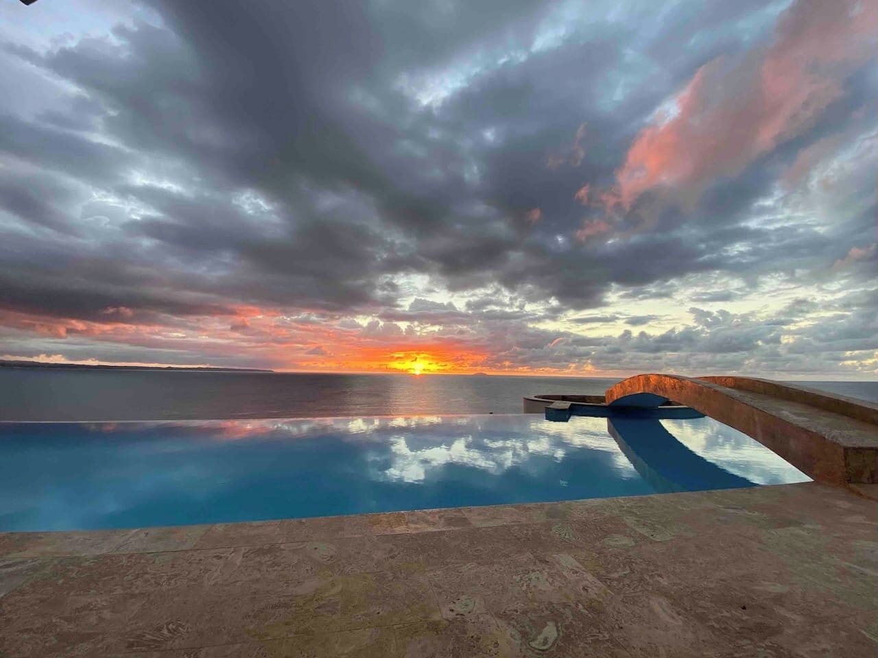 An infinity pool with a view of the sunset over the ocean.