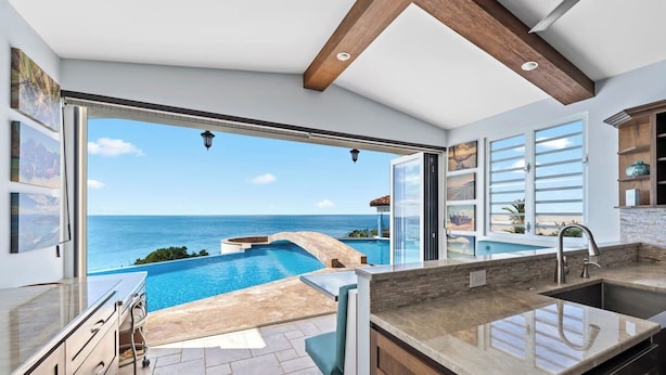 A modern kitchen with a large island, a built-in oven, and a view of a pool and ocean.