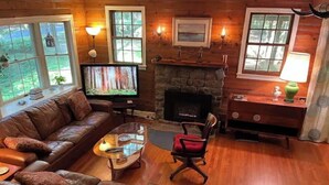 Ein gemütliches Wohnzimmer mit Ledersofa, Glastisch, Kamin und Fernseher.