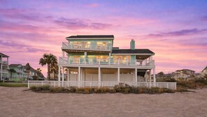 Een huis aan het strand met een balkon, een tweede verdieping en een overdekte veranda.
