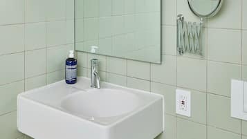 Un bagno con un lavandino bianco, uno specchio e uno scaffale con articoli da toilette.