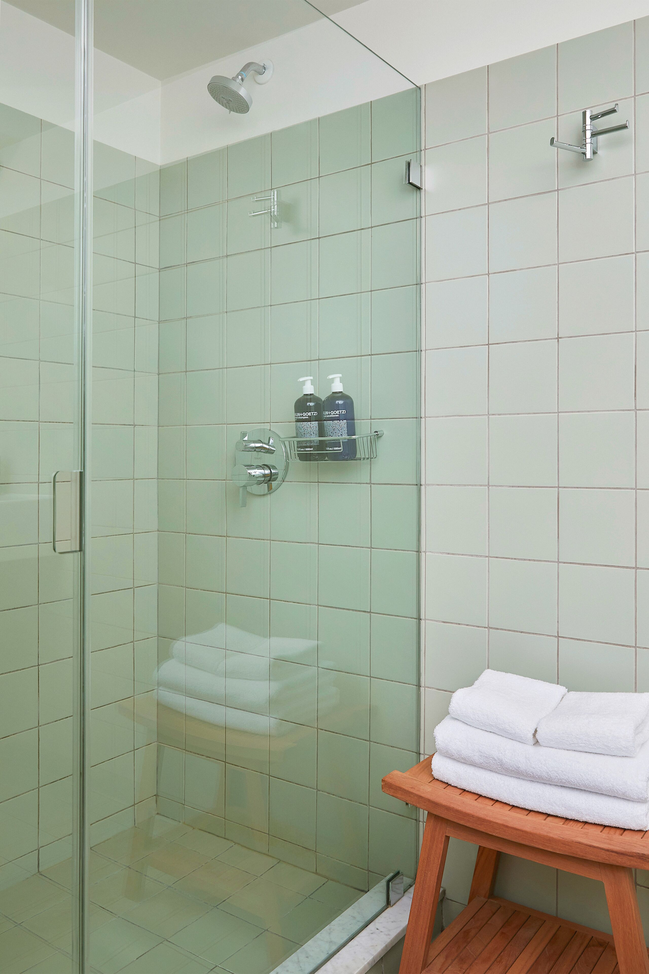 A glass-enclosed shower with a handheld showerhead, a soap dispenser, and a towel rack.