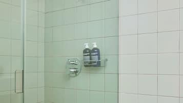 A glass-enclosed shower with a handheld showerhead, a soap dispenser, and a towel rack.