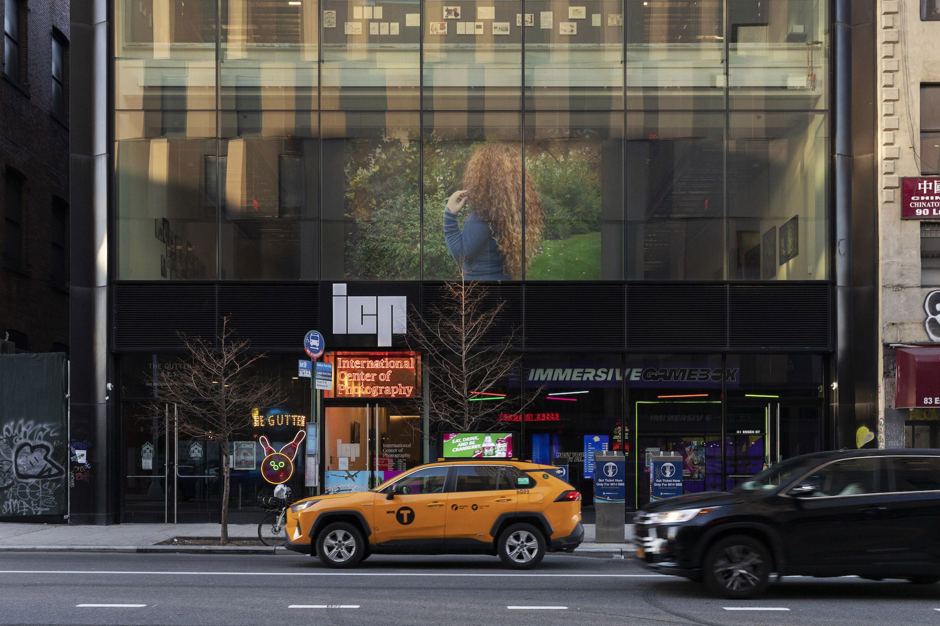 A modern building with a glass facade reflecting a person and greenery.