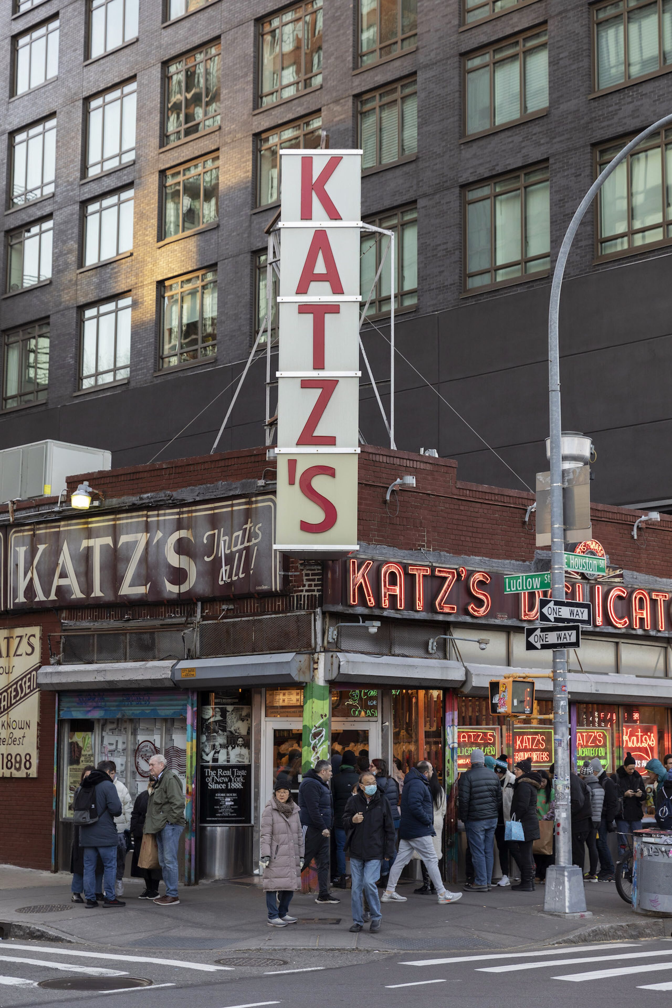Una calle concurrida con un llamativo letrero 'KATZ'S' y un edificio con numerosas ventanas.