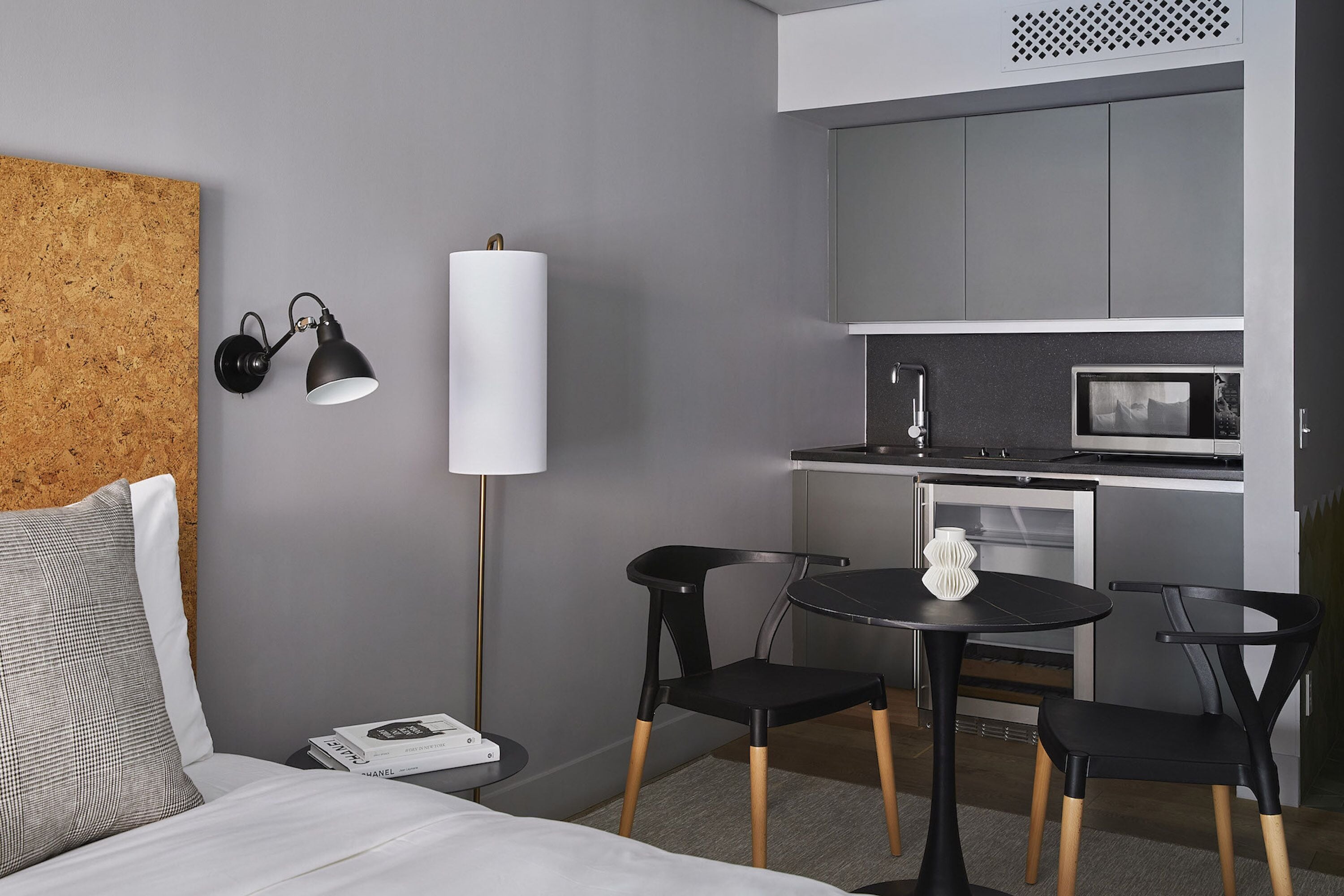 Una habitación de hotel moderna con cama, una pequeña mesa de comedor con sillas, microondas y kitchenette.