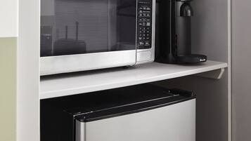 Una cucina compatta con forno a microonde integrato, macchina per il caffè e mini frigorifero.