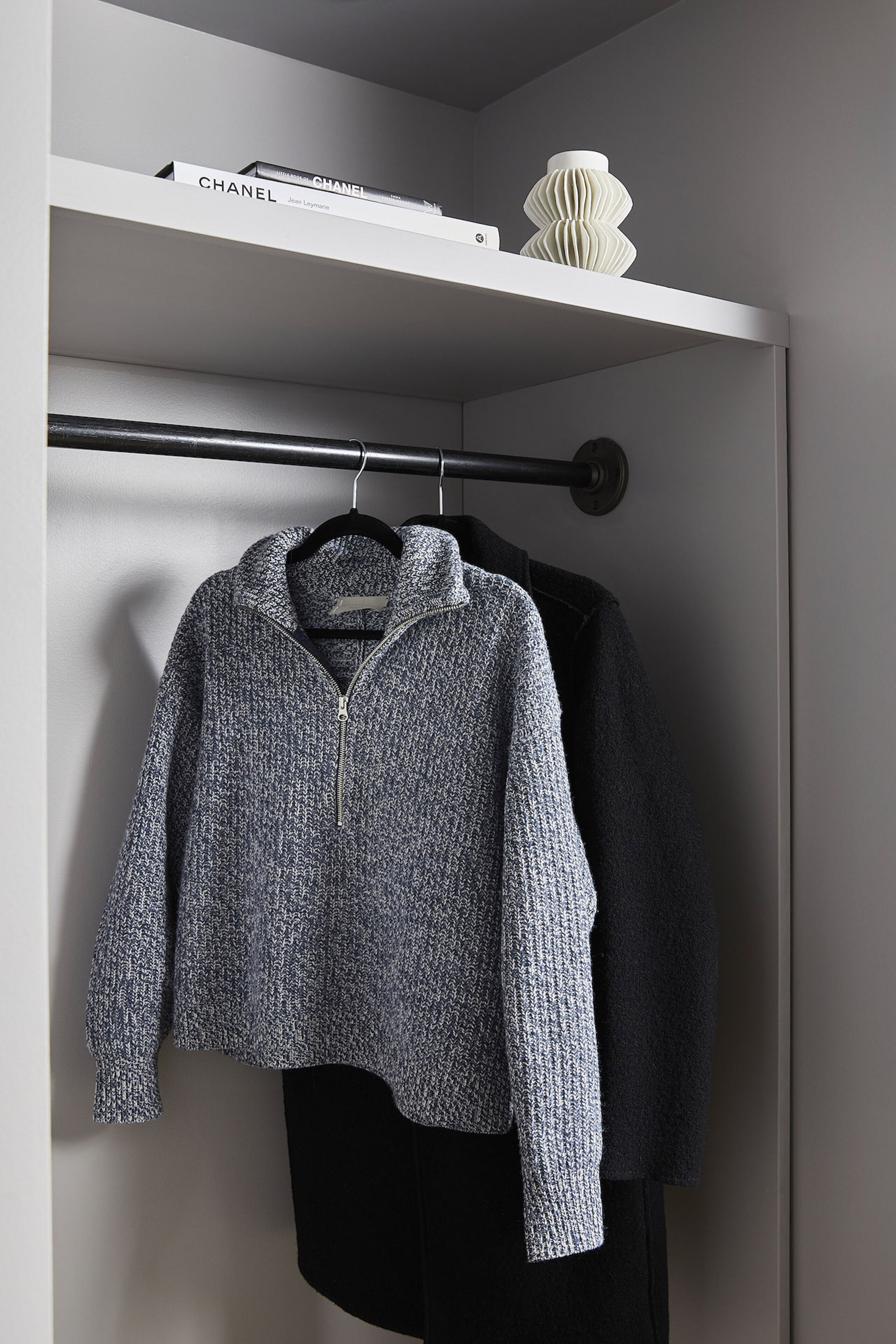 A closet with a hanging rod, a Chanel book, and a white vase.