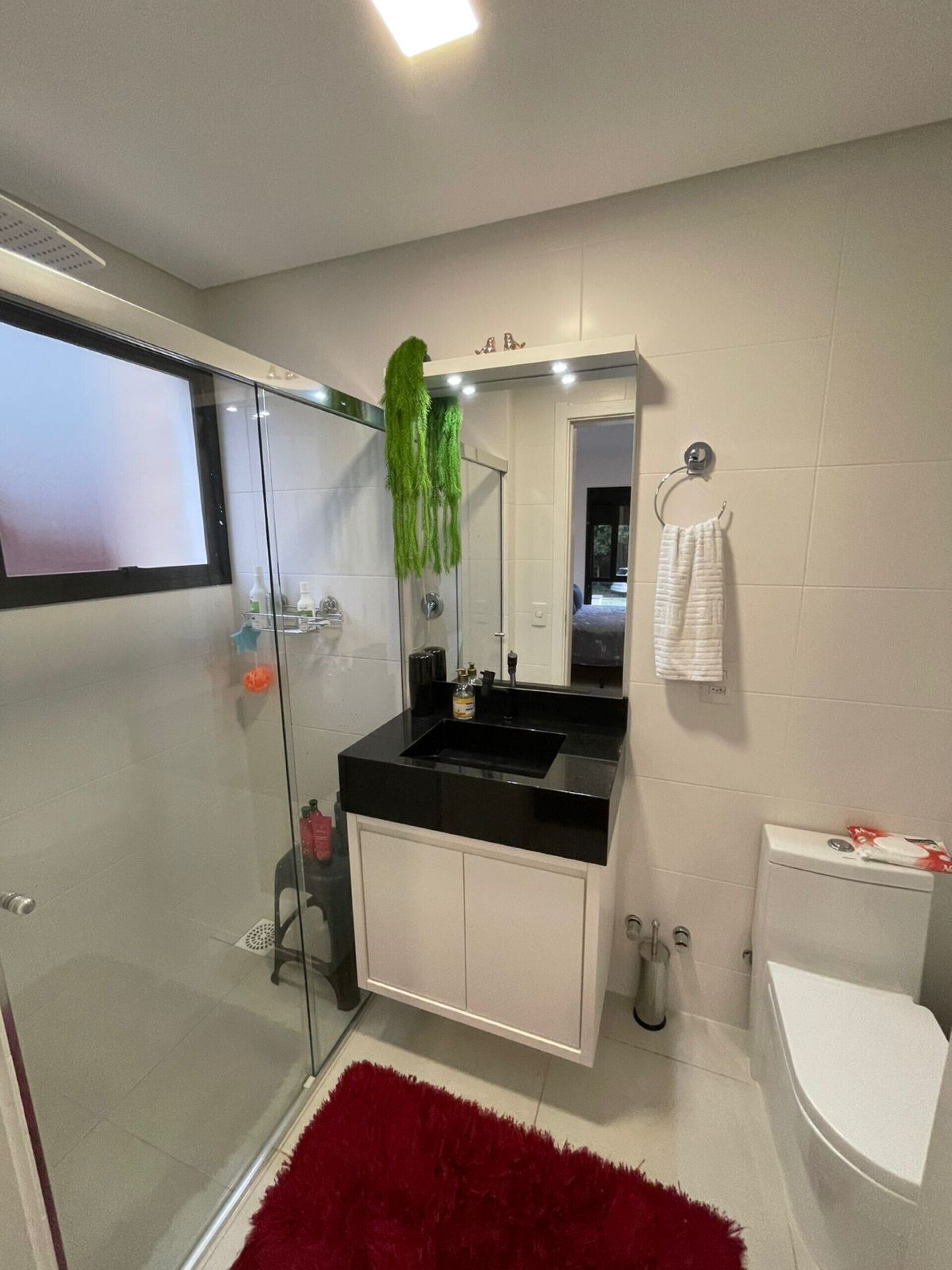A modern bathroom with a glass shower enclosure, a black countertop sink, a white toilet, and a red rug.
